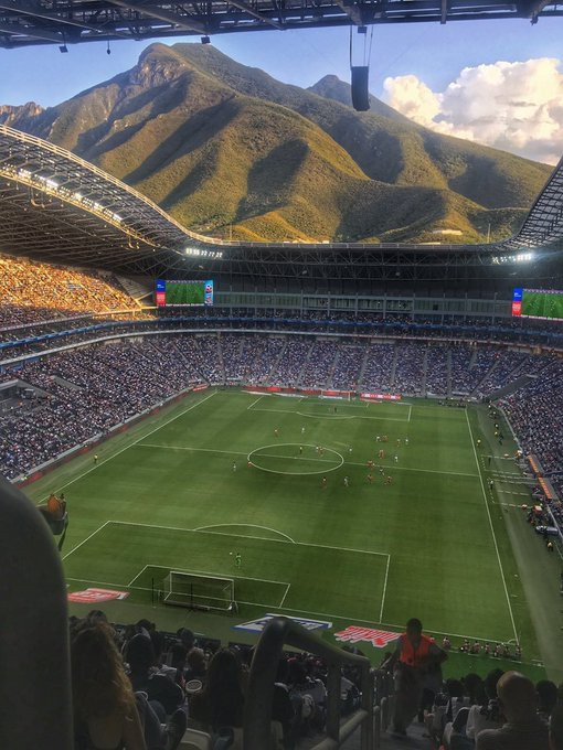 Crowded football stadium with green field and mountains in the background