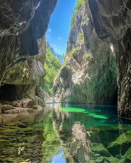 Rocky cave gorge with clear green water, reflections, and sunlight under a blue sky