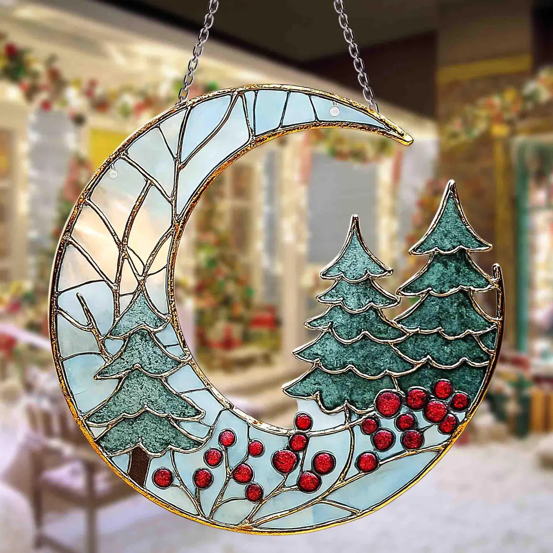 Crescent moon shaped stained glass suncatcher with evergreen trees and red berries hanging by silver chains