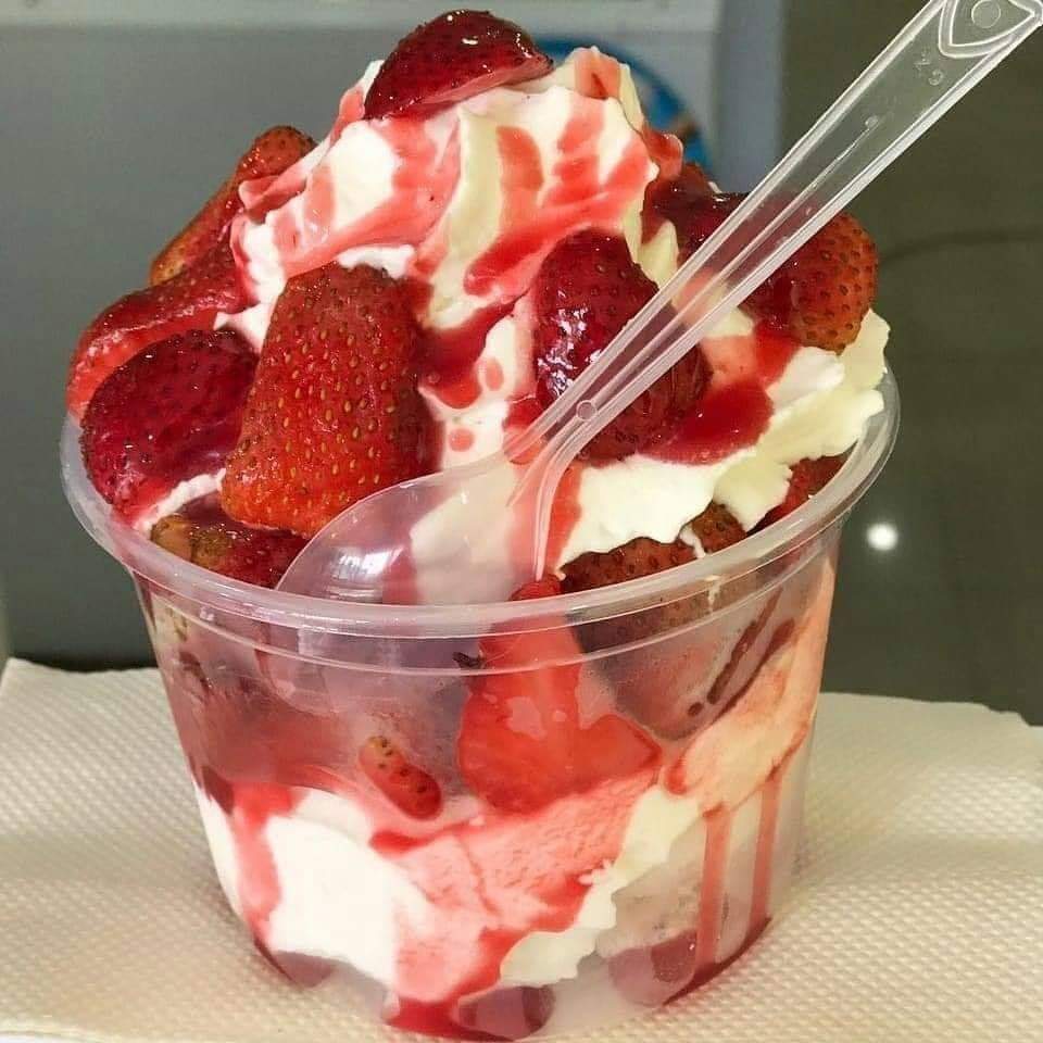Layered strawberry dessert with whipped cream and berry sauce in a clear cup