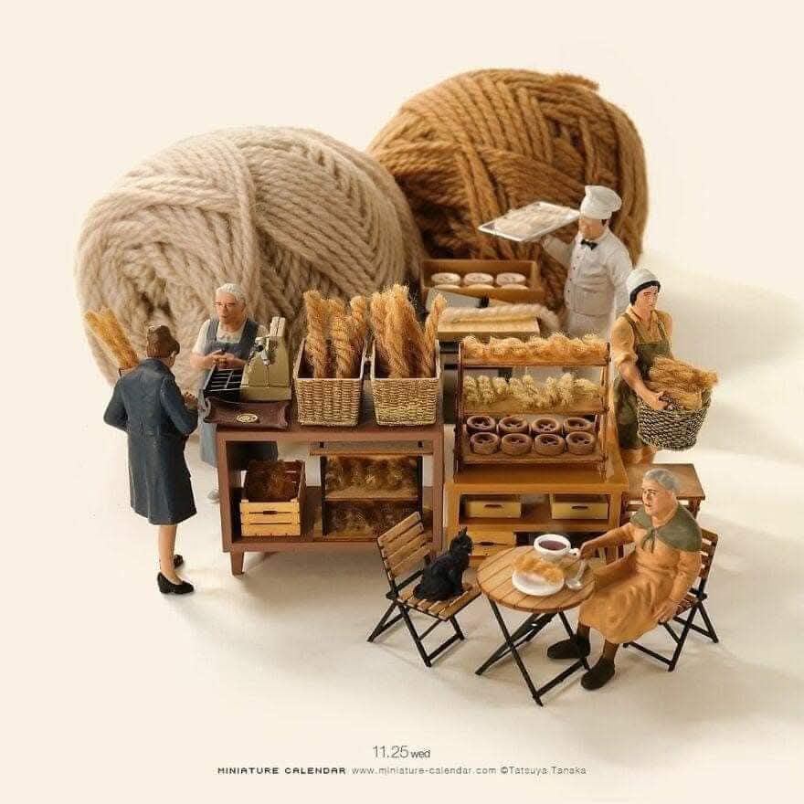 Miniature bakery scene with tiny people, bread shelves, tables, and two large balls of yarn