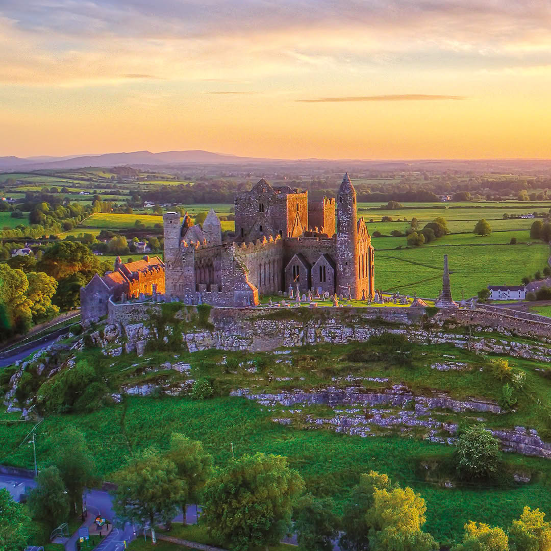 Aerial view of the Rock of Cashel ruins on a green hilltop in Ireland at sunset