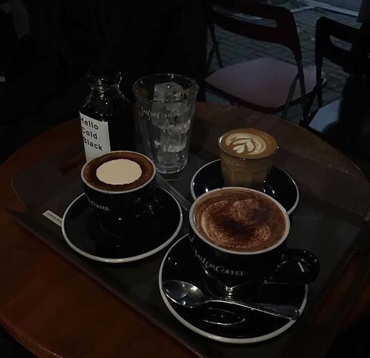 Tray with three coffee drinks, a water glass, and a small bottle on a dark cafe table