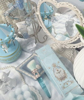 Flat lay of light blue and white coquette-style vanity items including mirrors, makeup brush, pearls, and carousel
