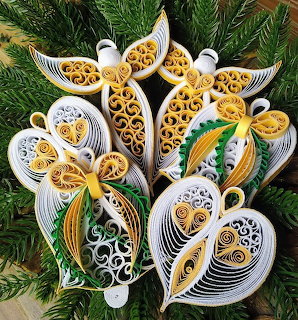 Handcrafted paper quilled ornaments in white and gold with decorative swirls on green pine branches