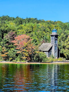 Old wooden lighthouse on a woded lakeshore with fall foliage and calm blue water