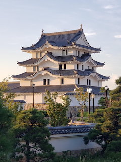 Japanese castle tower with layered roofs above trees and a stone wall