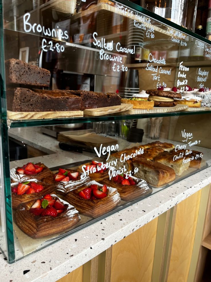 Glass cafe display case showing multiple tiers of brownies, cakes, and strawberry chocolate pastries on wooden boards