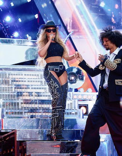 Female performer in black cowboy hat and sparkly outfit on stage with a male dancer holding a disco ball