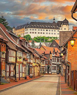 Historic German village street with half-timbered houses and a hilltop building at sunset