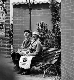 Elderly couple sitting together on a bench under an awning in a black and white photograph