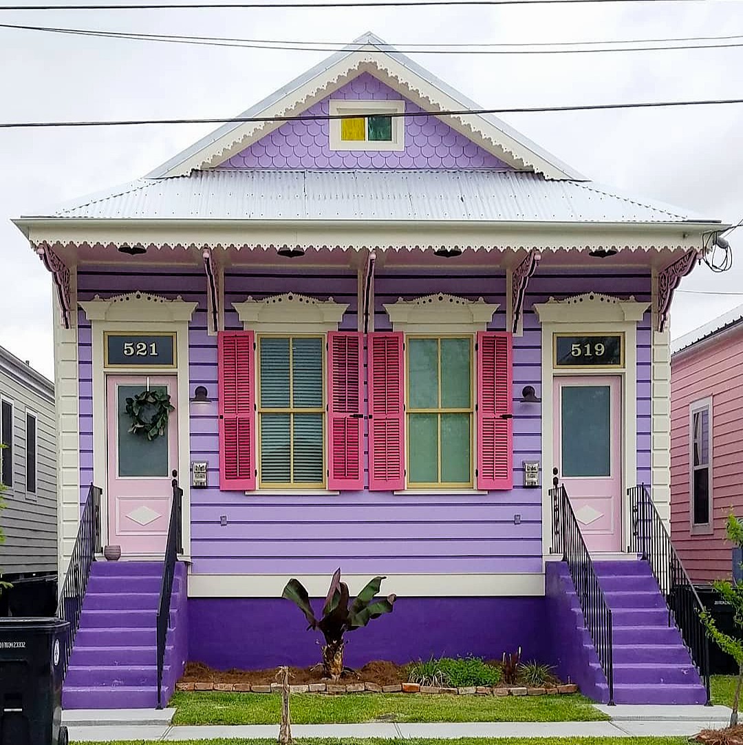 Purple wooden cottage with pink shutters, metal roof, and symmetrical front stairs
