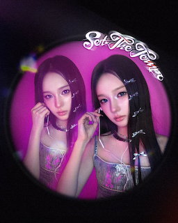 Two young women with long dark hair posing through a circular fisheye lens against a pink backdrop