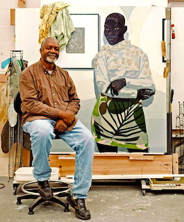 Artist Kerry James Marshall sitting on a stool in his art studio with a large figurative painting behind him