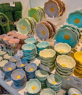Stacks of flower-shaped ceramic bowls and plates in pastel colors displayed in a store