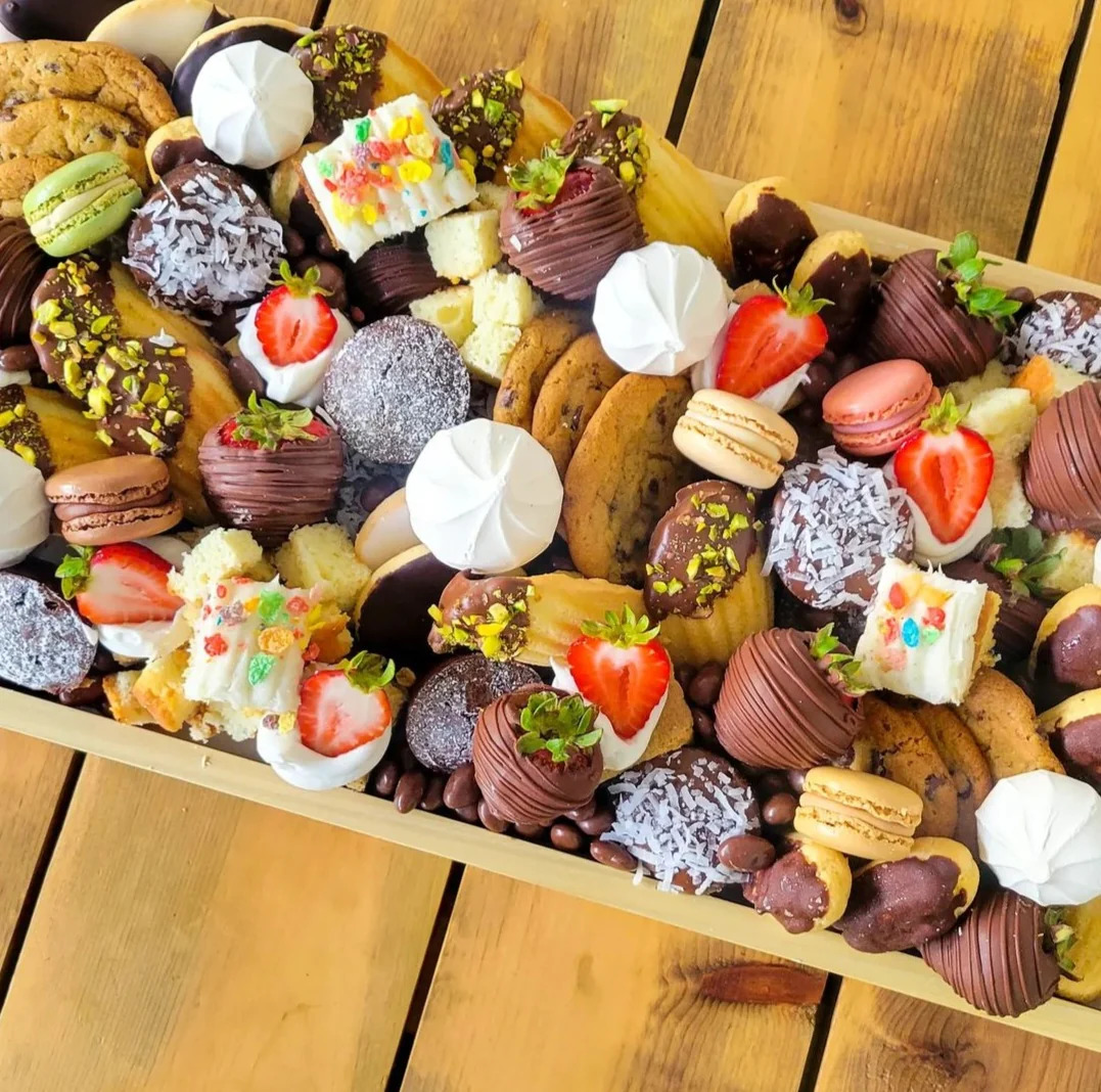 Assorted desserts including macarons, chocolate strawberries, and pastries on a wooden board
