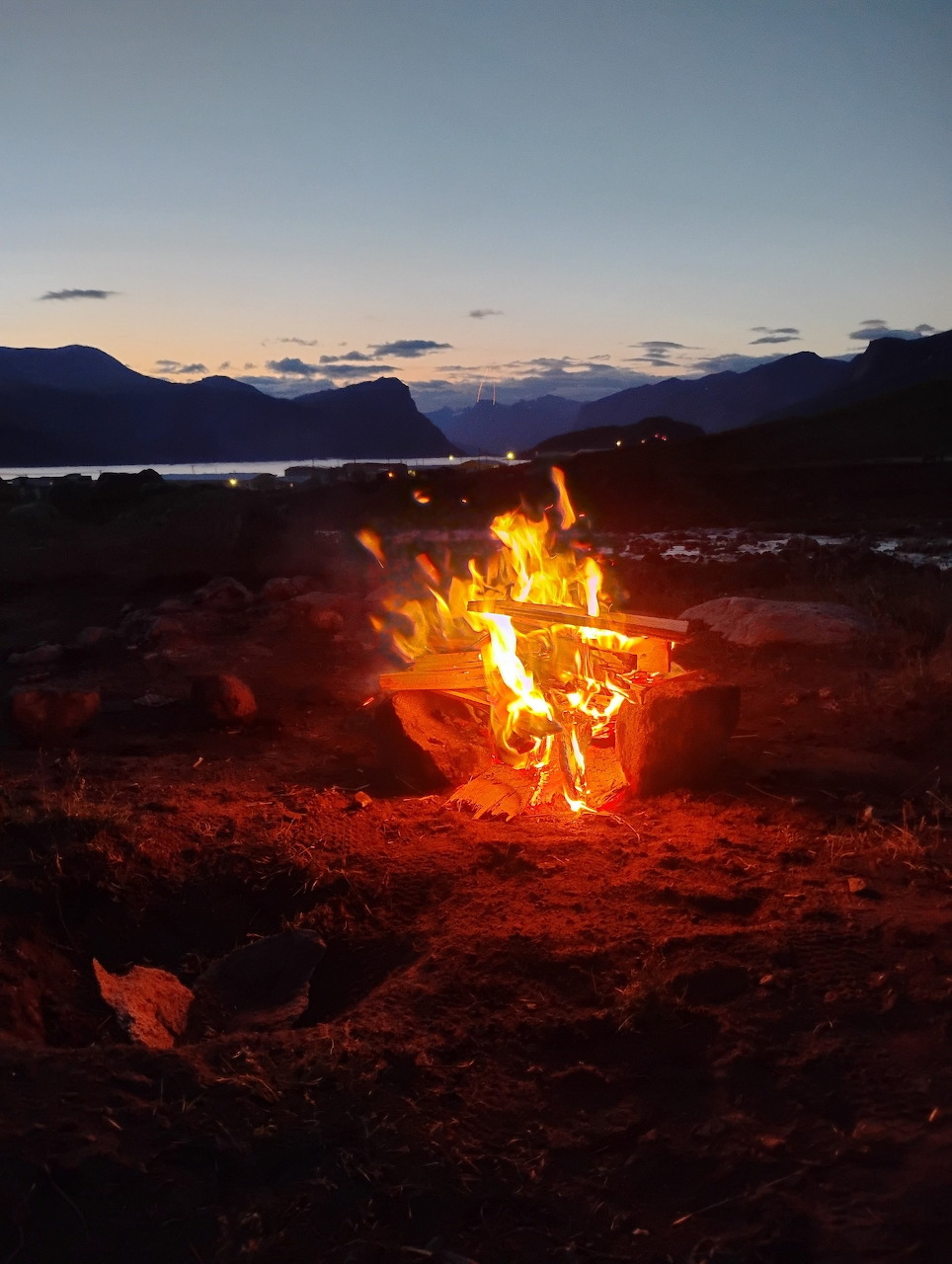 Bright campfire burning at dusk with Arctic mountains and water in the background, Pangnirtung, Nunavut.