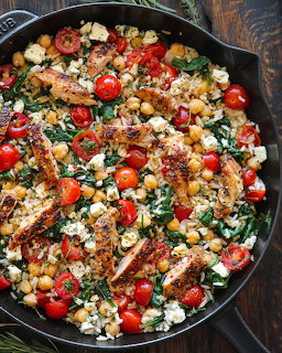 Cast iron skillet with grilled chicken strips, cherry tomatoes, chickpeas, spinach, and feta cheese