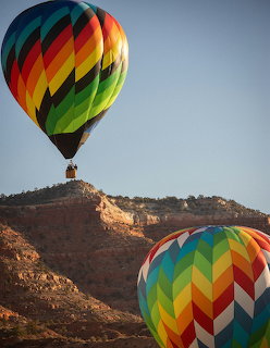Two colorful hot air balloons flying above a rocky desert hillside