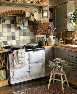 Cozy country kitchen with white AGA stove, green cabinets, brick arch, and colorful tile backsplash