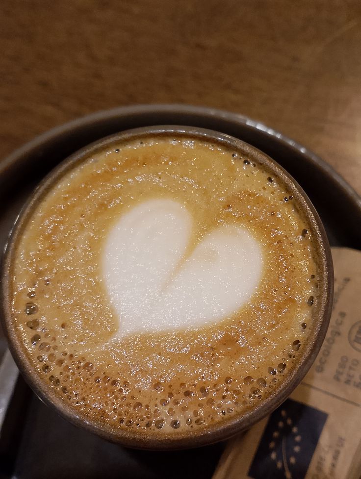 Overhead view of a latte with white heart foam art in a black cup on wood table