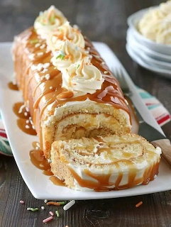Sliced caramel cake roll with cream filling, caramel drizzle, whipped cream, and nuts on white platter