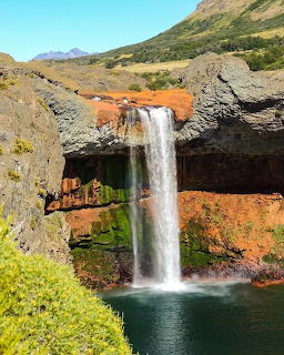 Tall waterfall dropping over orange volcanic cliffs into a green pool, Salto del Agrio, Neuquén, Argentina
