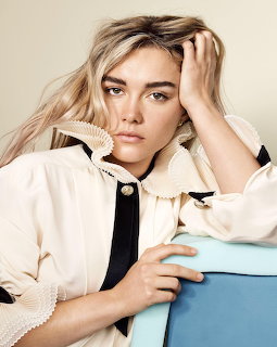 Florence Pugh portrait in a cream ruffled blouse, resting her arm on a blue chair