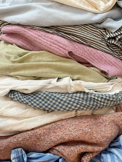 Pile of folded clothes in pastel colors including pink knit, gingham, and striped fabrics