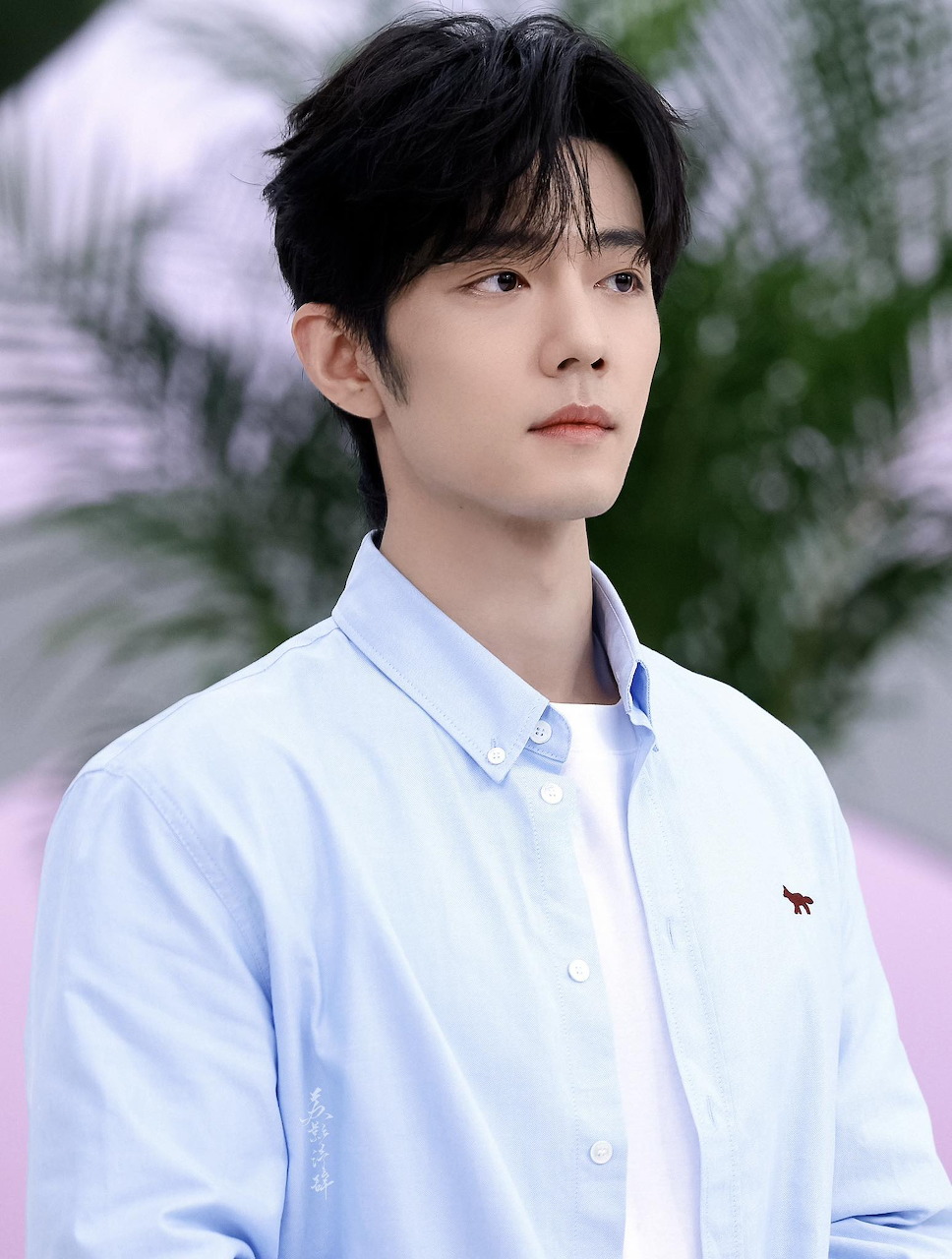 Young East Asian man in light blue shirt looking upward, soft pink background