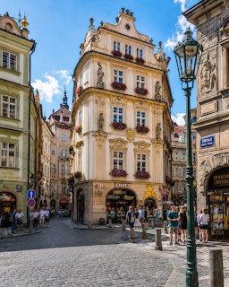 Historic Prague street with ornate buildings, cobblestones, pedestrians, and a vintage lamp post