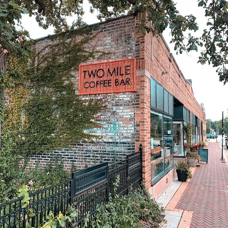 Brick coffee bar exterior with a Two Mile Coffee Bar sign, ivy-covered wall, and sidewalk