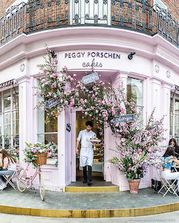 Pink Peggy Porschen Cakes storefront decorated with abundant pink flowers and a person in the doorway