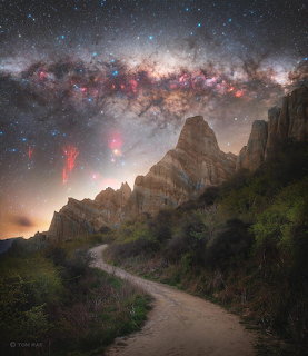 Winding dirt path between rocky cliffs under the Milky Way with red lightning sprites in the night sky