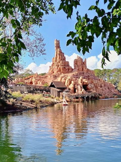 Red rock mountain theme park ride with water reflection and trees