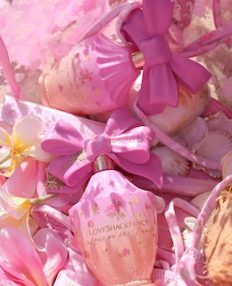 Pink perfume bottles with floral designs and satin bows among shells and flowers on sand