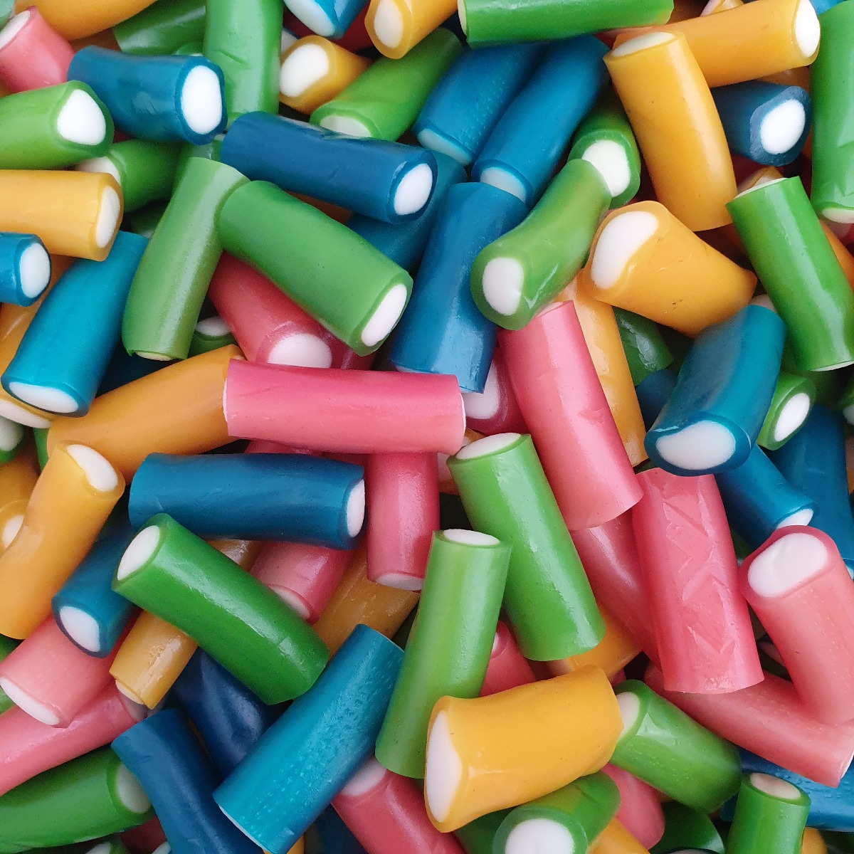 Colorful cylindrical candy rolls with white ends in pink, blue, green, orange, and yellow scattered together
