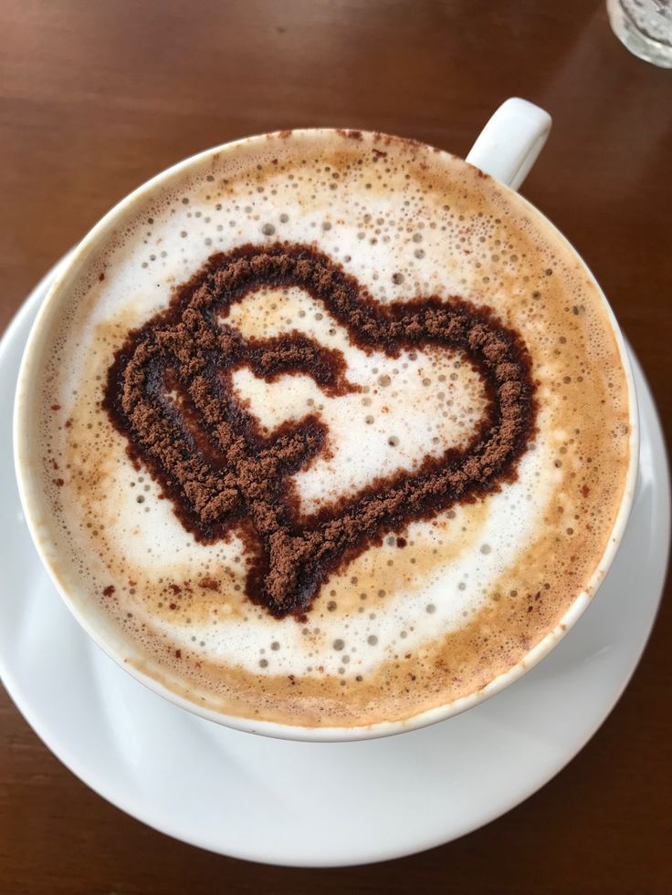 White coffee cup with heart latte art on foam, viewed from above on wooden surface