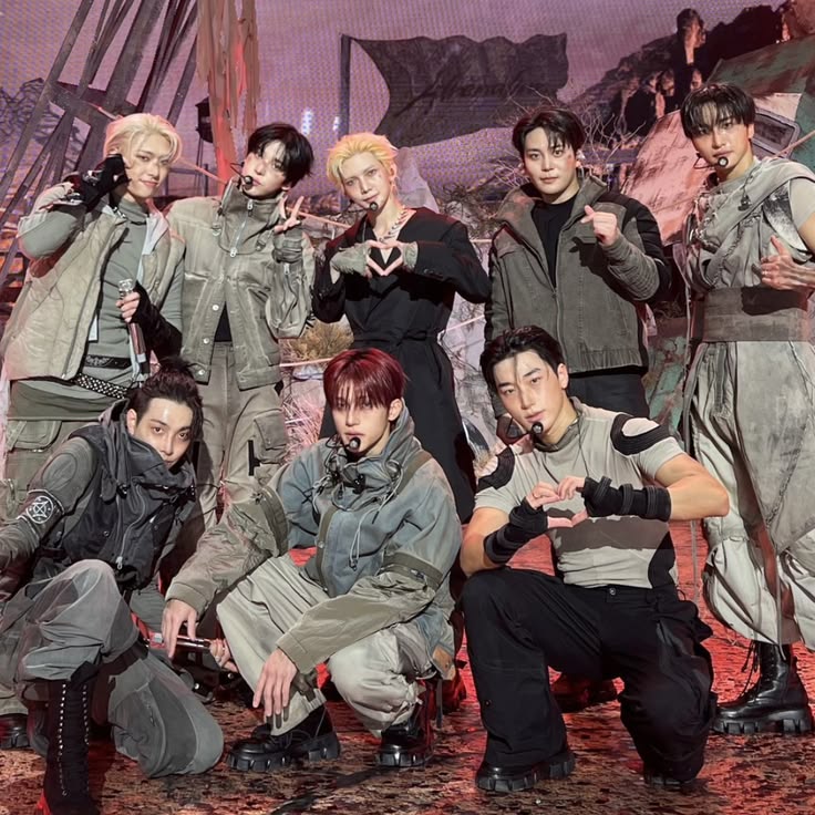 Eight young men in gray and black street fashion posing in an industrial urban setting with chains