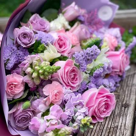 Pink roses and purple lilac bouquet wrapped in purple paper on a wooden table