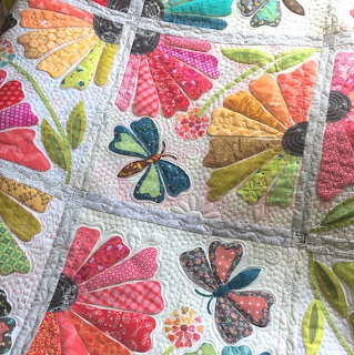 Handmade quilt with colorful fabric flower petals and butterfly appliqués on white quilted fabric