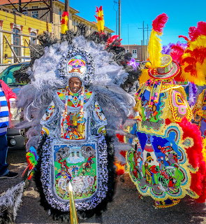 Three people wearing ornate Mardi Gras Indian costumes with massive feathered headdresses in purple, white, and rainbow colors