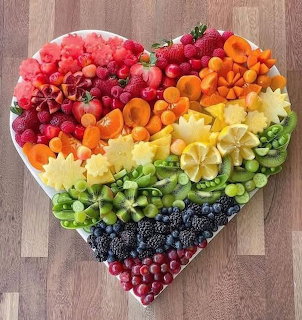 Heart-shaped arrangement of colorful fresh fruits in rainbow gradient on wooden cutting board