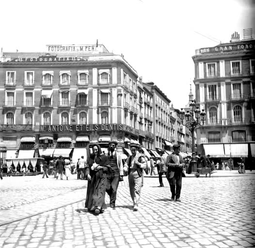 Black-and-white photo of an old Madrid square with people walking between historic buildings