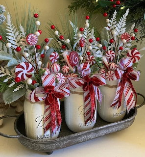 Three mason jars decorated with Christmas greenery, candy canes, berries, and red striped bows on a metal tray