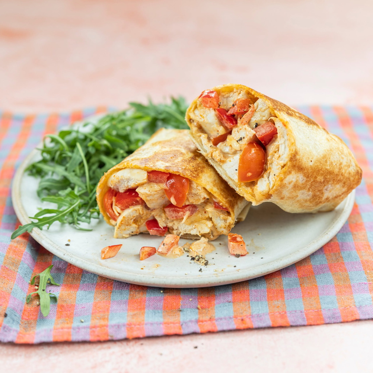Two toasted wrap halves with chicken and red pepper filling on a plate beside arugula