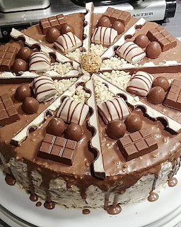 Round chocolate cake decorated with chocolate bars, round bonbons, and white chocolate shavings