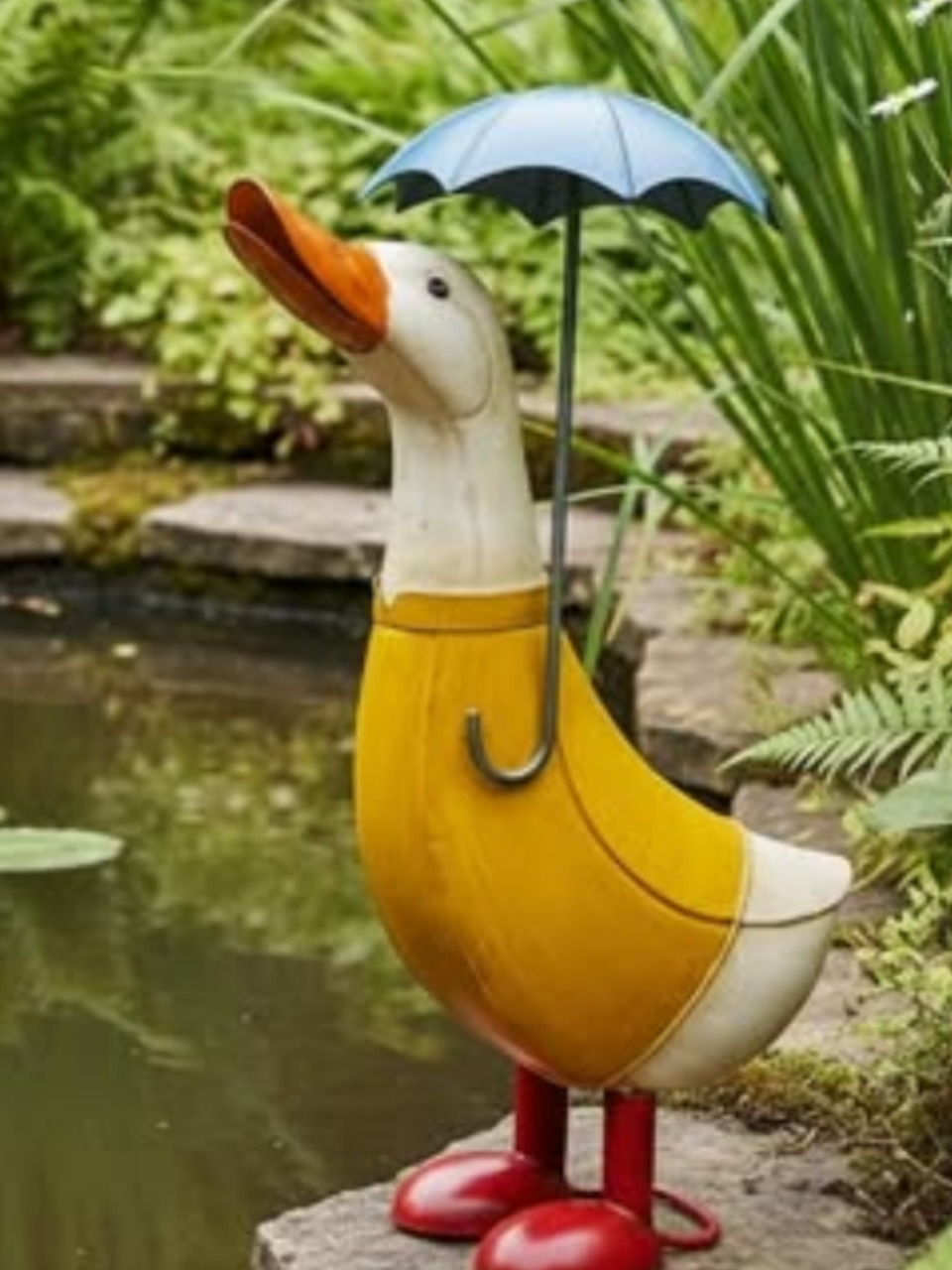Duck garden statue in a yellow raincoat holding an umbrella beside a pond