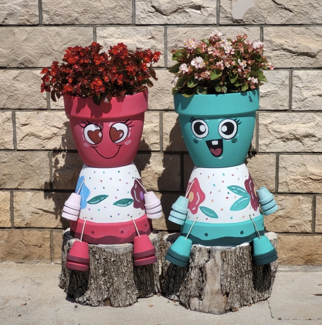 Two cartoon-style painted flower pots with flowers, sitting on tree stumps by a stone wall.