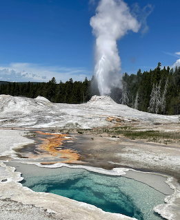 Old Faithful geyser erupting with steam rising high, colorful hot springs in foreground, Yellowstone National Park